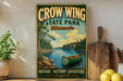 A vintage-style sign for Crow Wing State Park in Minnesota, featuring a canoe on a lake surrounded by pine trees.