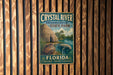 A vintage-style metal sign for Crystal River State Park in Florida, featuring a manatee and a thatched-roof hut, is displayed on a wooden wall.