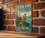 A vintage-style metal sign for Crystal River State Park in Florida, featuring an illustration of a manatee and a thatched-roof hut, set against a brick wall.