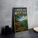 A vintage-style sign for Cumberland Mountain State Park, featuring a scenic mountain landscape with a river and a cliff.