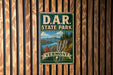 A vintage-style metal sign for Vermont State Park, featuring a scenic landscape with mountains, forests, and a river.