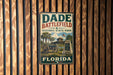 A vintage metal sign for Dade Battlefield Historic State Park in Florida, featuring an illustration of a cannon and a building, mounted on a wooden wall.