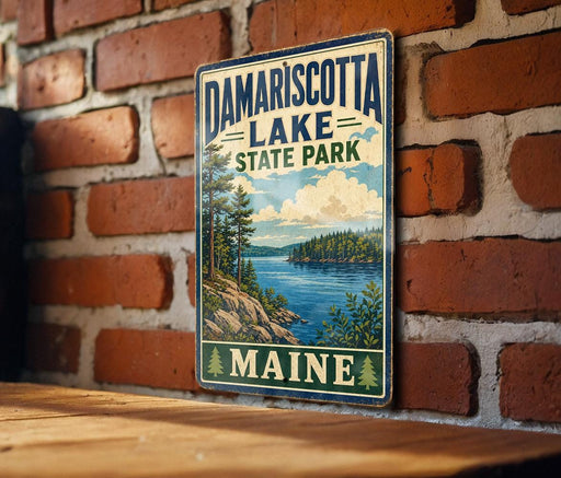 A vintage metal sign for Damariscotta Lake State Park in Maine, featuring a scenic landscape with a lake, mountains, and pine trees.