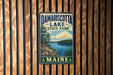 A vintage-style metal sign for Damariscotta Lake State Park in Maine, featuring a scenic landscape with a lake, mountains, and pine trees.