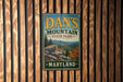 A vintage metal sign for Dan's Mountain State Park in Maryland, featuring a scenic mountain landscape.