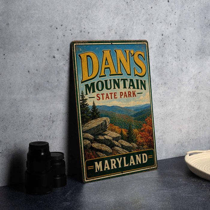A vintage metal sign for Dan's Mountain State Park in Maryland, featuring a scenic mountain landscape with autumn foliage.