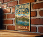 A vintage metal sign for Dankworth Pond State Park in Arizona, featuring a scenic landscape with a heron and a pond surrounded by mountains.