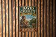 A vintage metal sign for David Crockett State Park in Tennessee, featuring an illustration of a man with a rifle and the text "Preserving History Naturally" and "Hiking, Camping, Fishing".