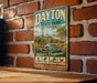 A vintage metal sign for Dayton State Park, Nevada, featuring a scenic landscape with mountains, a river, and various outdoor activities such as hiking, fishing, and wildlife viewing.