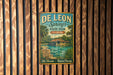 A vintage-style metal sign for De Leon Springs State Park in Florida, featuring a tropical landscape with palm trees and a body of water.