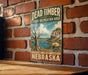 A vintage-style metal sign for Dead Timber State Recreation Area in Nebraska, featuring a scenic landscape with a lake and mountains.