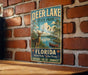 A vintage-style metal sign for Deer Lake State Park in Florida, featuring a scenic illustration of a deer, a canoe, and a lake surrounded by palm trees.