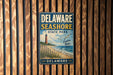 A vintage metal sign for Delaware Shore State Park, featuring a lighthouse and beach scene, is displayed on a wooden wall.