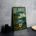 A vintage metal sign for Delaware State Park, featuring a scenic landscape with a lake, trees, and a sailboat, is displayed on a gray concrete surface.