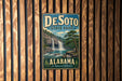A vintage metal sign for DeSoto State Park in Alabama, featuring a waterfall and forest landscape.