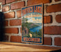 A vintage-style metal sign for Devil's Lake State Park in Wisconsin, featuring a scenic landscape with a lake, mountains, and a tree.