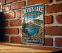A vintage metal sign for Devil's Lake, a state recreation area in Oregon, featuring a scenic landscape with a lake, mountains, and pine trees.