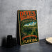 A vintage-style metal sign for Devil's Millhopper Geological State Park in Florida, featuring a scenic image of the park's natural landscape.