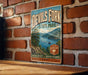 A vintage-style sign for Devil's Fork State Park, featuring a scenic landscape with a lake and mountains, mounted on a brick wall.