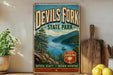 A vintage-style metal sign for Devil's Fork State Park, featuring a scenic landscape with a lake, mountains, and a boat.