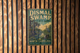 A vintage-style metal sign for Dismal Swamp State Park in North Carolina, featuring a bird and a swampy landscape.