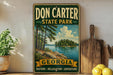 A vintage-style sign for Don Carter State Park in Georgia, featuring a scenic landscape with a lake and trees.