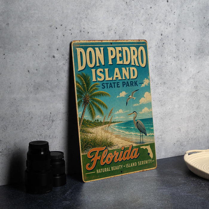 A vintage-style sign for Don Pedro Island, Florida, featuring palm trees, a beach, and a bird, is displayed on a gray concrete surface.