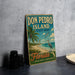A vintage-style sign for Don Pedro Island, Florida, featuring palm trees, a beach, and a bird, is displayed on a gray concrete surface.