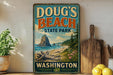 A vintage-style sign for Doug's Beach State Park in Washington, featuring a scenic landscape with a rocky outcrop, beach, and pine trees.