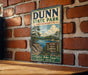 A vintage-style metal sign for Dunn State Park in Massachusetts, featuring a scenic landscape with a lake and mountains.