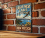 A vintage-style sign for Eagle Nest Lake State Park in New Mexico, featuring a scenic landscape with mountains, trees, and a bird in flight.