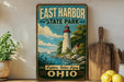 A vintage-style sign for East Harbor State Park in Ohio, featuring a lighthouse and a scenic landscape.