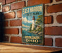 A vintage-style metal sign for East Harbor State Park in Ohio, featuring a lighthouse and a scenic landscape.