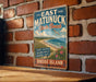 A vintage-style metal sign for East Matunuck State Beach, featuring a beach scene with a bird flying overhead and text describing the location.