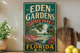 A vintage-style sign for Eden Gardens State Park in Florida, featuring a scenic illustration of a bridge, palm trees, and colorful flowers.