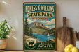 A vintage-style sign for Edness K. Wilkins State Park in Wyoming, featuring a scenic mountain landscape with a lake and a sailboat.