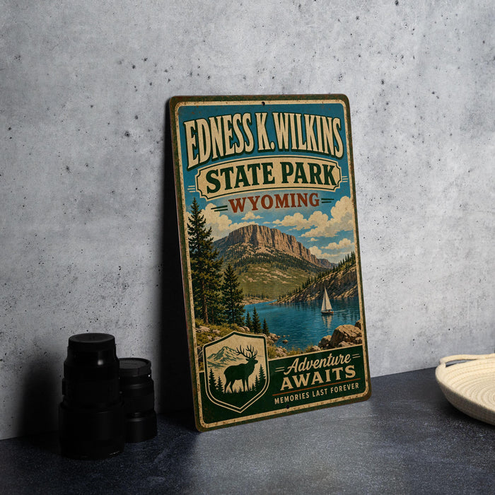 A vintage-style metal sign for Edness K. Wilkins State Park in Wyoming, featuring a scenic landscape with mountains, a lake, and a sailboat.