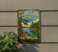 A vintage-style metal sign for Ellah Clark State Park in Georgia, featuring a scenic landscape with a river and pine trees.