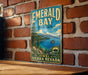 A vintage-style sign for Emerald Bay State Park, featuring a scenic landscape with mountains, a lake, and pine trees.