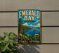 A vintage-style sign for Emerald Bay State Park, featuring a scenic landscape with mountains, a lake, and pine trees.