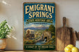 a vintage-style sign for the Emigrant Springs State Heritage Area in Oregon, depicting a covered wagon and a stone bridge in a scenic landscape.