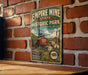 A vintage-style metal sign for Empire Mine State Historic Park in California, featuring an illustration of the historic site with a red brick wall in the background.