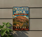 A vintage-style metal sign for the Enchanted Rock State Natural Area in Texas, featuring a scenic illustration of the rock formation and desert landscape.