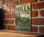 A vintage metal sign for F. Gilbert Hills State Forest in Massachusetts, featuring a scenic landscape with pine trees and a lake.