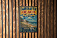 A vintage metal sign for Fair Haven Beach State Park in New York, featuring a beach scene and text promoting the park's natural beauty, sandy beaches, scenic views, relaxation, and swimming opportunities.