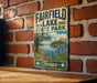 A vintage-style sign for Fairfield Lake State Park in Texas, featuring a scenic landscape with a lake, trees, and flowers.
