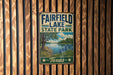 A vintage metal sign for Fairfield Lake State Park in Texas, featuring a scenic landscape with a lake, trees, and flowers.
