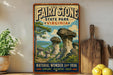 a vintage-style sign for Fairy Stone State Park, Virginia, with a scenic illustration of rock formations and a lake. The sign is displayed on a shelf next to a wooden cutting board and a potted plant.