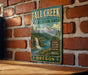 A vintage metal sign for the Fall Creek State Recreation Area in Oregon, featuring a scenic mountain landscape with a waterfall.