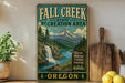 a vintage-style sign for the Fall Creek State Recreation Area in Oregon, with a mountain landscape and a waterfall.